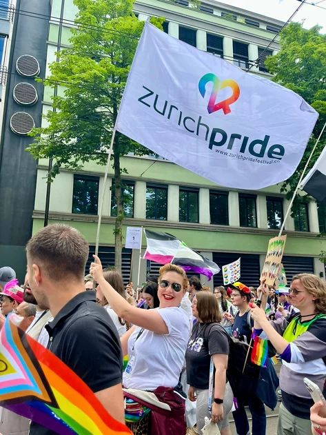 Julia A. Müller läuft mitten in einem Umzug mit und schenkt eine Fahne mit der Aufschrift zurich pride.