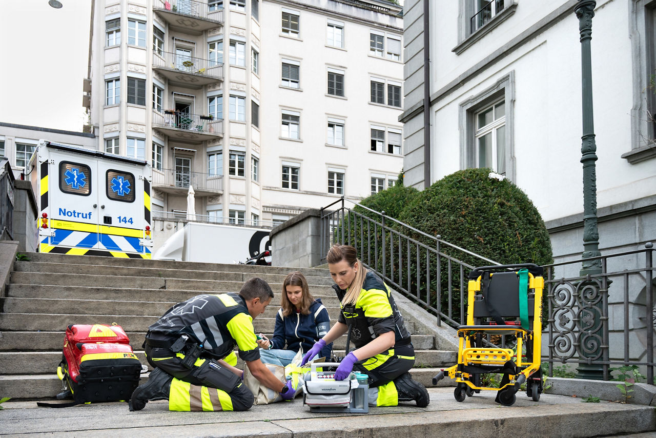 Rettungssanitäter*innen versorgen eine Patientin auf einer Treppe.