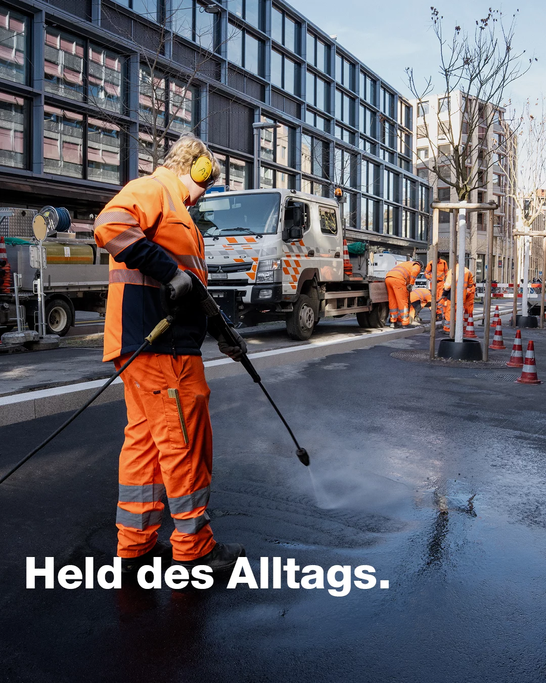 Held des Alltags. Ein Lernender Betriebsunterhalt reinigt in oranger Uniform die Strasse.