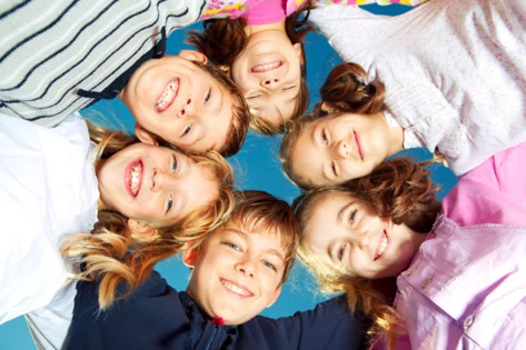 Sechs Kinder strecken die Köpfe zusammen und lachen in die Kamera.
