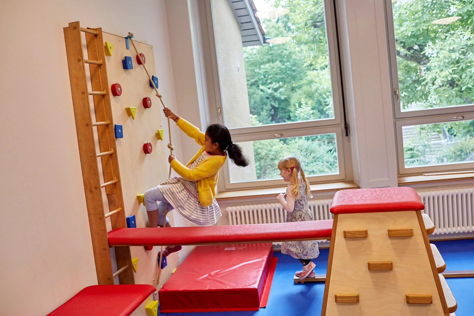 Mädchen klettert an Kletterwand im Kindergarten hoch.