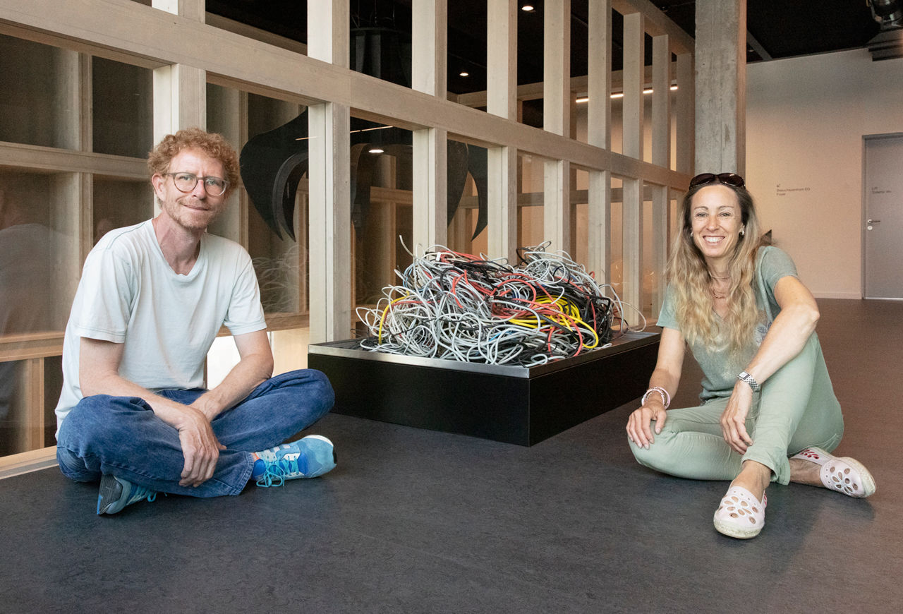 Sara Burgess und Nicolas Esseiva im Schneidersitz um die von ihnen ausgewählte Installation aus gebündelten Kabeln