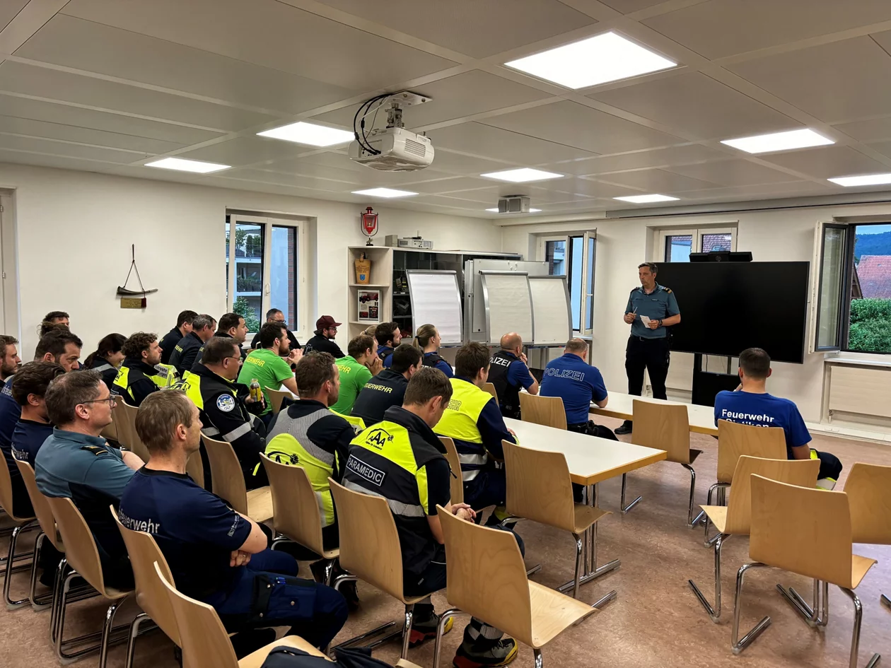 Teilnehmer*innen der Fliesswasserrettungs-Übung nehmen in einem Schulungsraum am Debriefing teil.