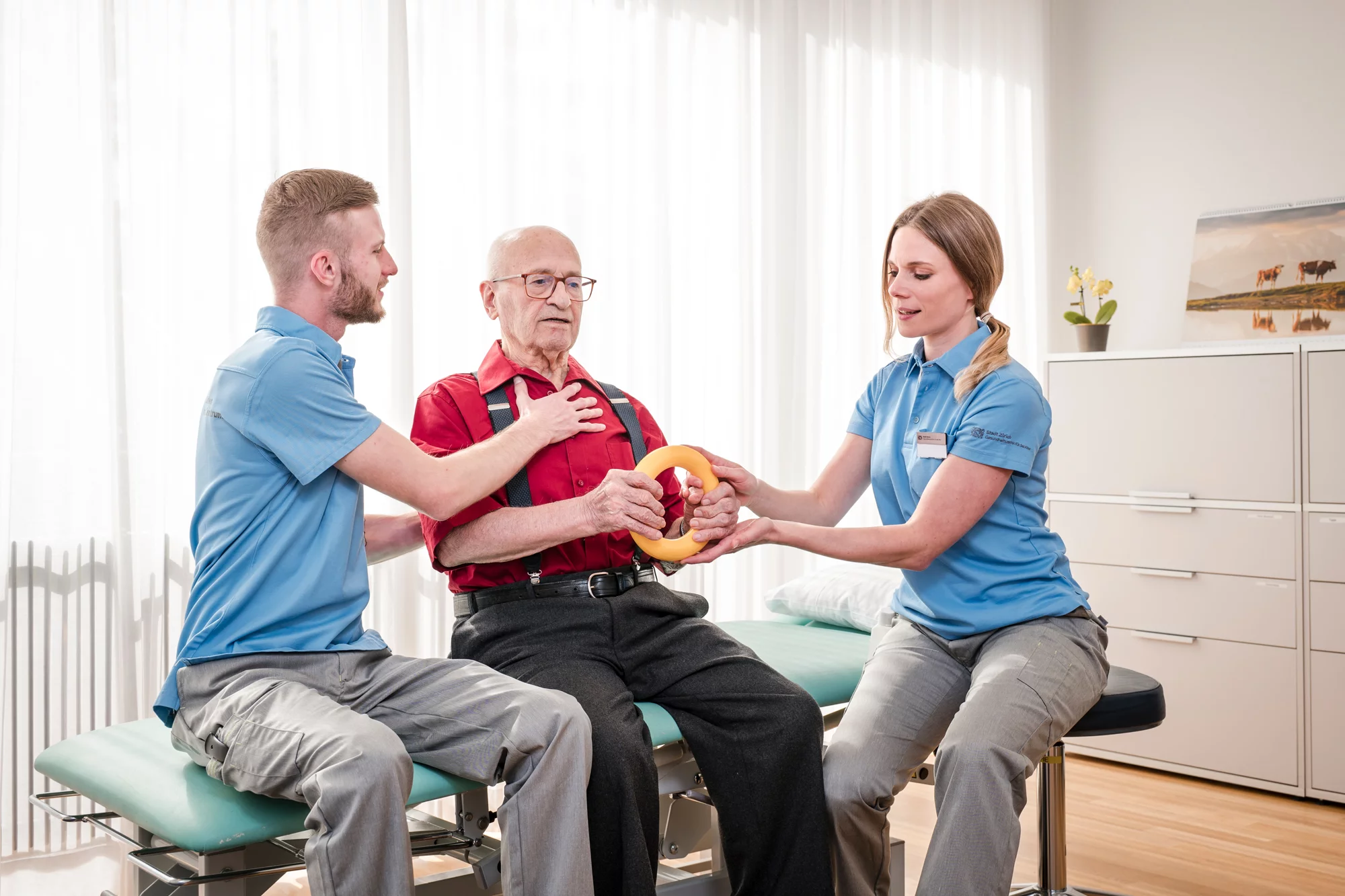 Zwei Dipl. Aktivierungsfachpersonen HF in Ausbildung führen eine Übung mit einem Bewohner auf einer Therapieliege durch.