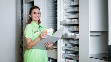 Mitarbeitende der Pflege steht vor der Apotheke.