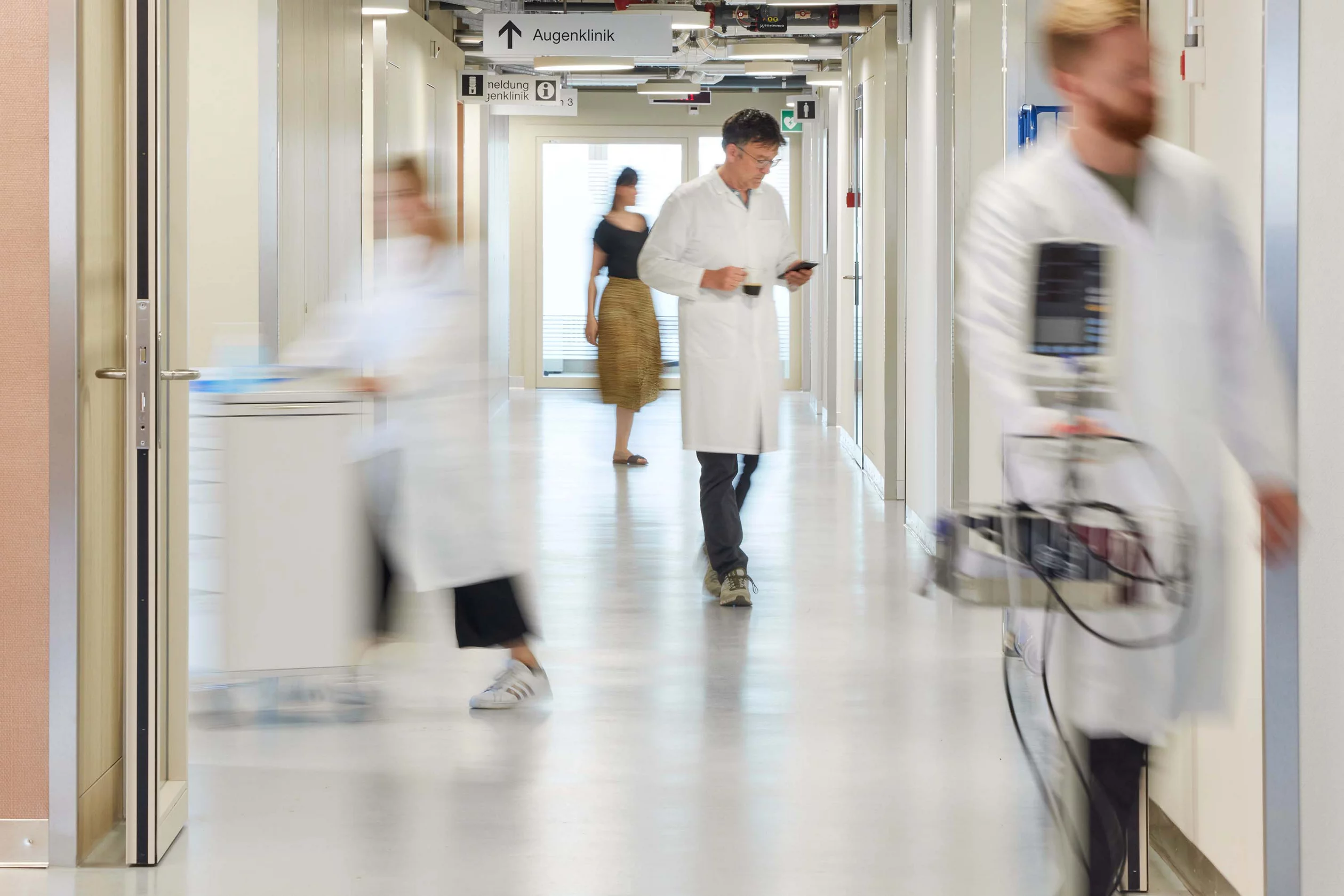 Belebter Gang in einer Klinik mit vier Personen darauf
