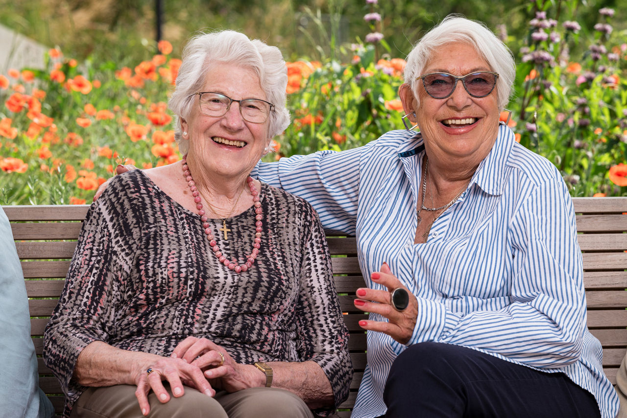 Zwei Gäste im Gesundheitszentrums für das Alter Bombach umarmen sich auf einer Sitzbank im Garten.