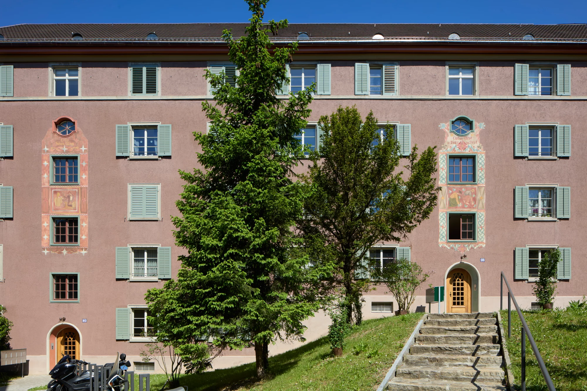 Fassade einer Wohnsiedlung  mit einem Treppenaufgang und zwei Bäumen davor