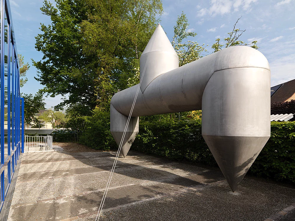 Plastik, die auf zwei dicken Beinen steht und in eine scharfe Spitze mündet