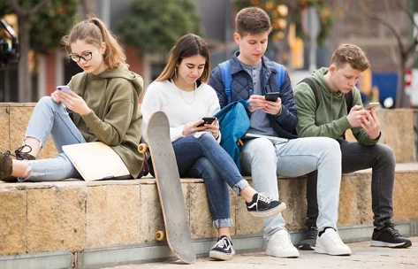 Zwei jugendliche Mädchen und zwei jugendliche Jungen sitzen auf einer Steintreppe und alle haben ein Handy in der Hand.