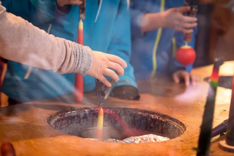 Eine Kinderhand taucht vorsichtig einen Docht ins heisse Wachs.