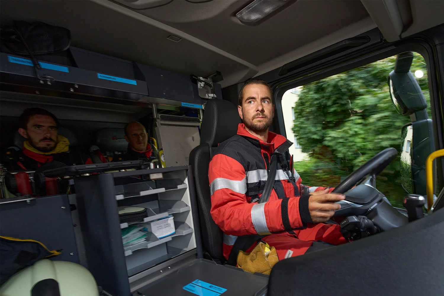 Drei Berufsfeuerwehrmänner in einem Feuerwehrfahrzeug