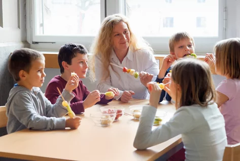 Fünf Kinder und eine Betreuerin essen Fruchtspieschen.