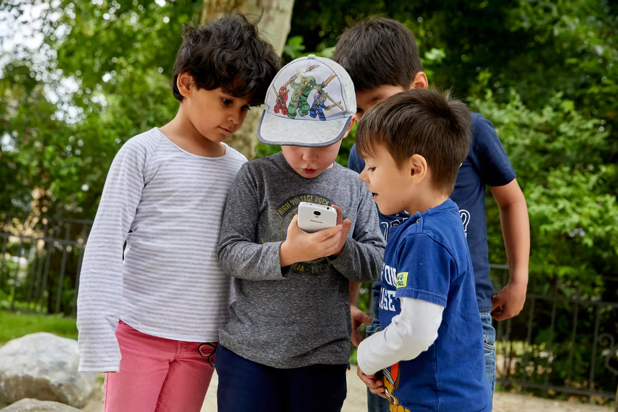 Vier Jungen schauen draussen auf ein Handy, welches der Mittlere in seinen Händen hält.