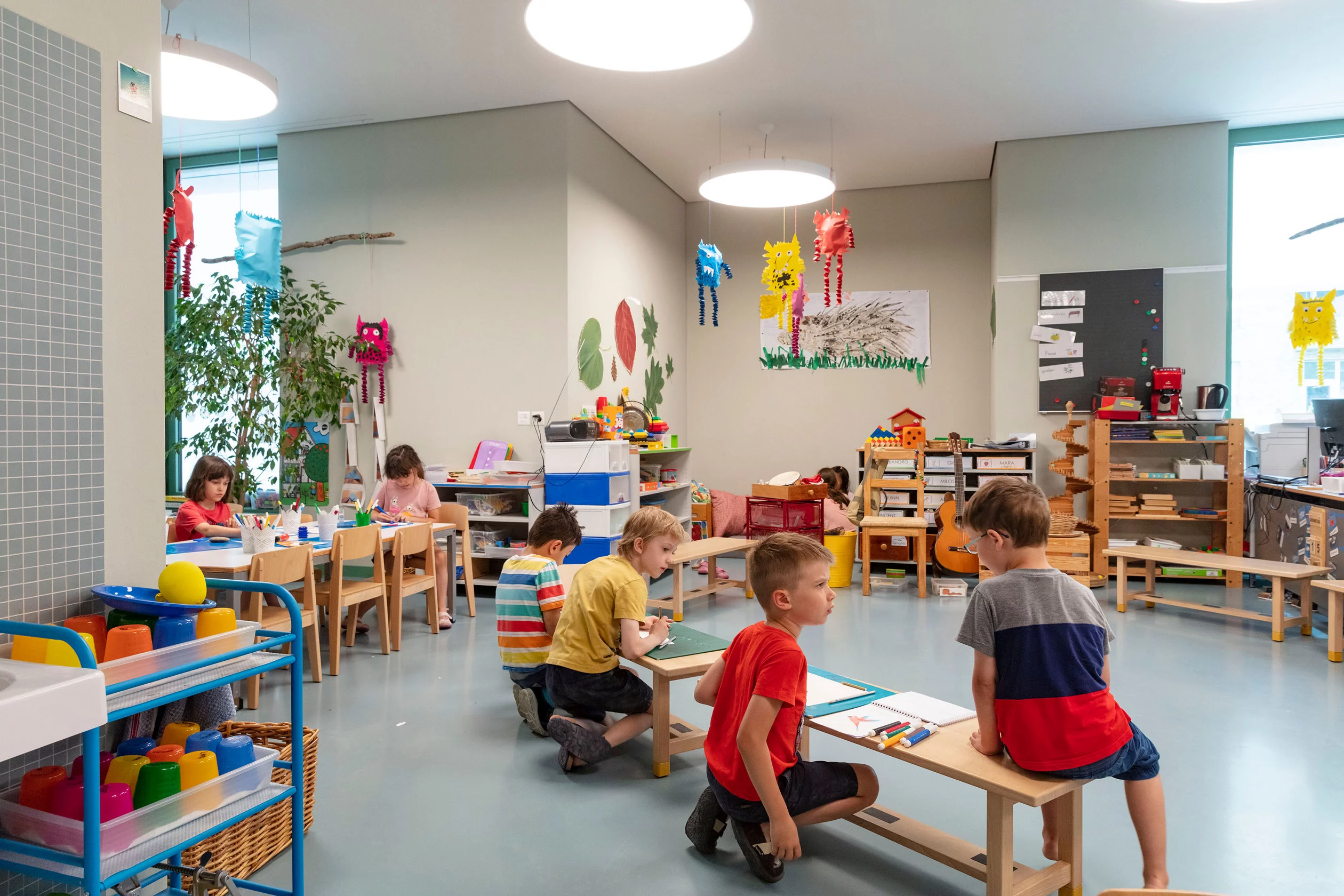 Kindergartenlokal mit Stuhlkreis und malenden Kindern.
