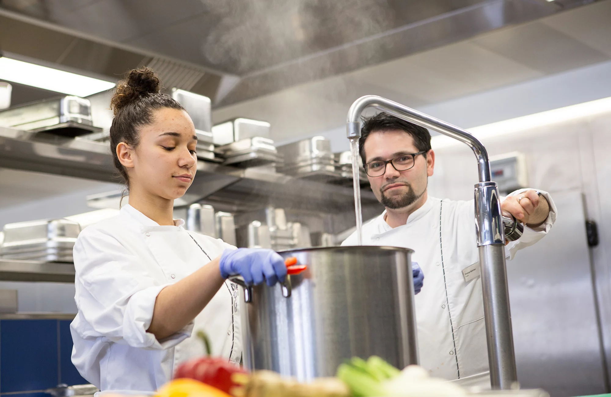 Eine Köchinnen in Ausbildung füllt eine Pfanne mit Wasser.