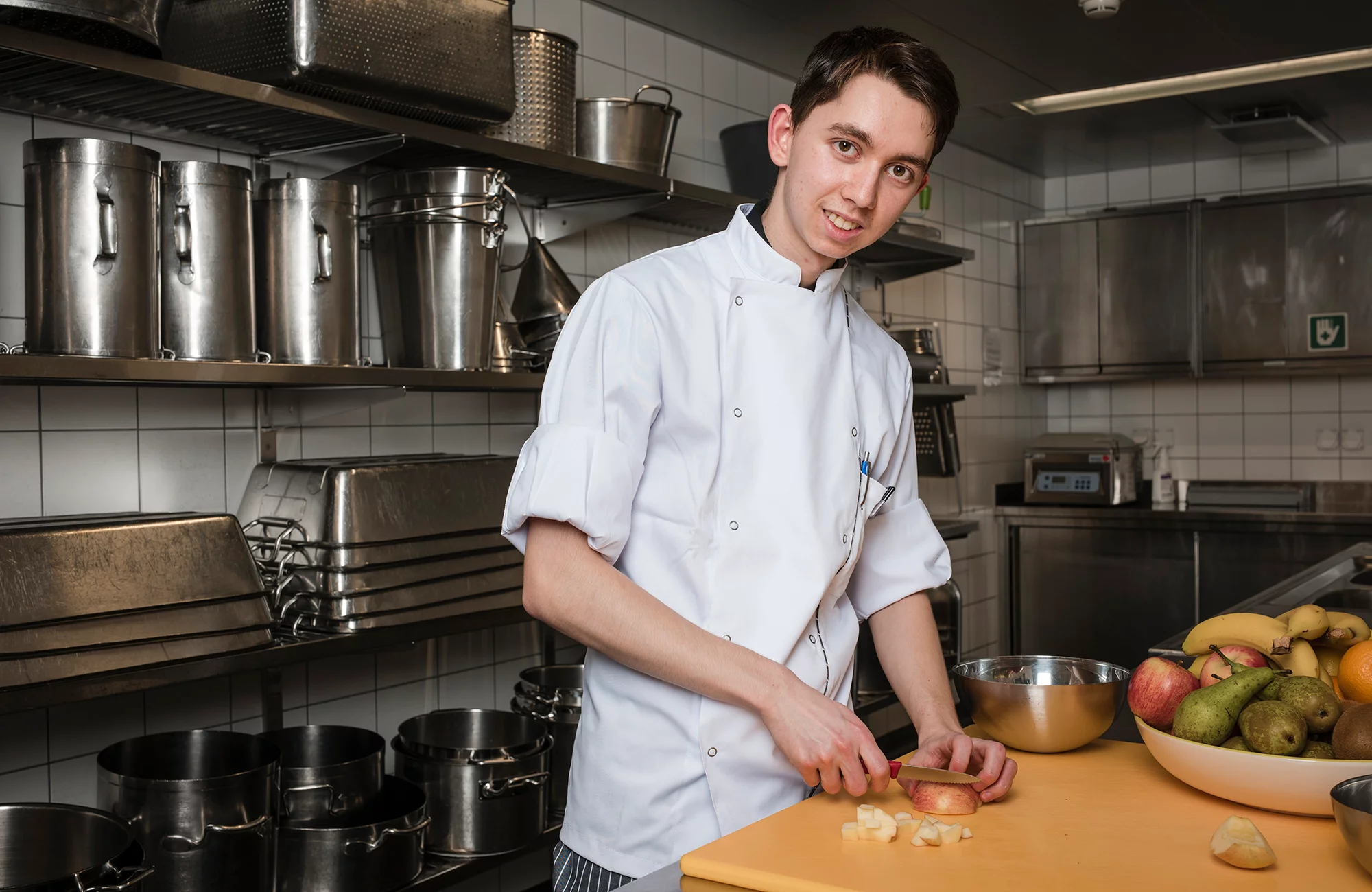 Küchenangestellter in Ausbildung schneidet in der Küche verschiedene Früchte.
