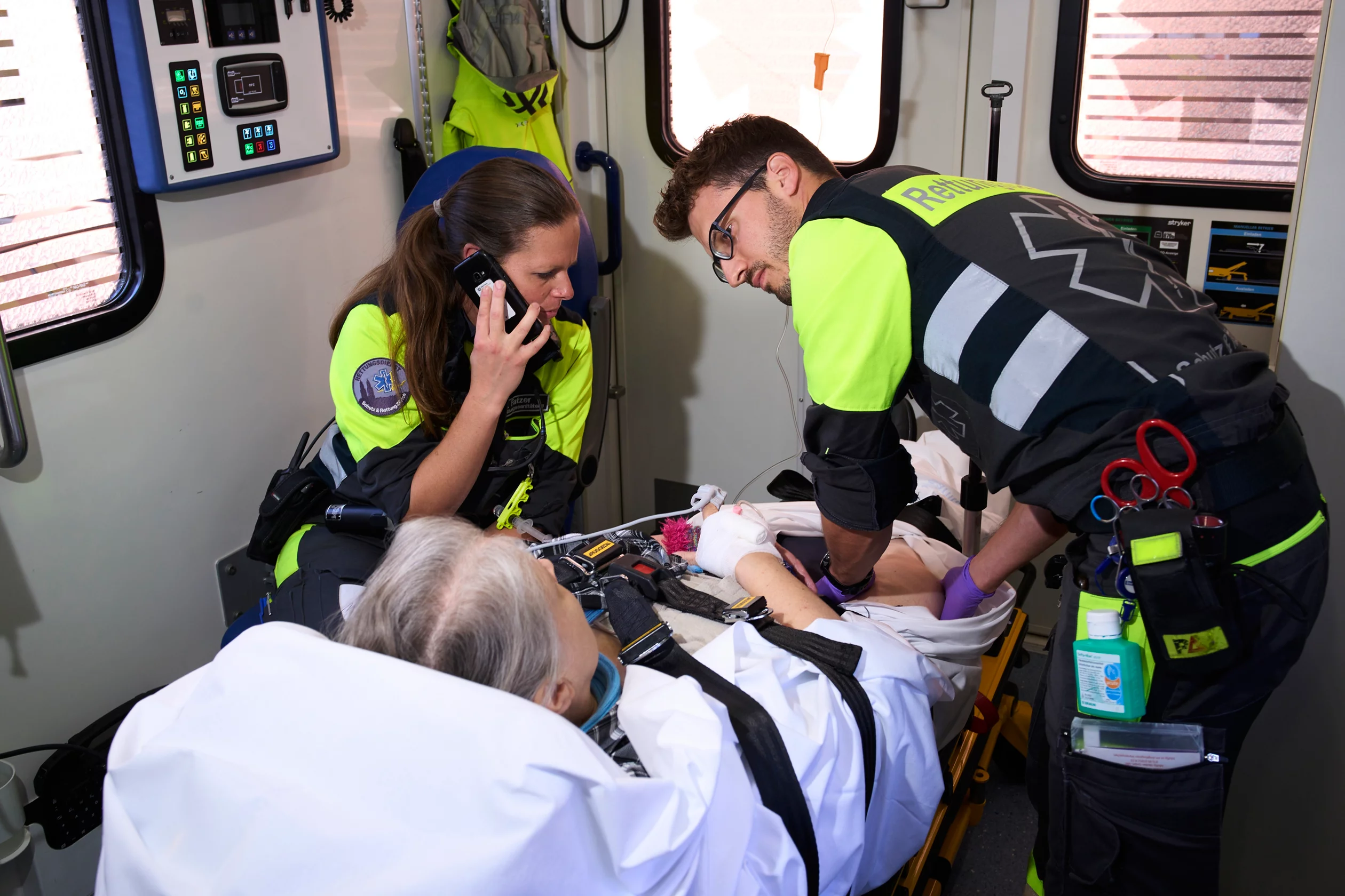 Zwei Rettungssanitäter*innen untersuchen in einem Rettungswagen eine Patientin