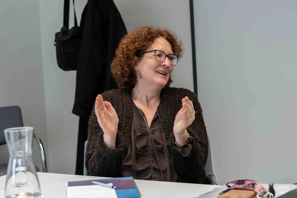 Meret Brunnschweiler, eingefangen im Gespräch, sitzt während des Interviews an einem Tisch und gestikuliert mit den Händen.