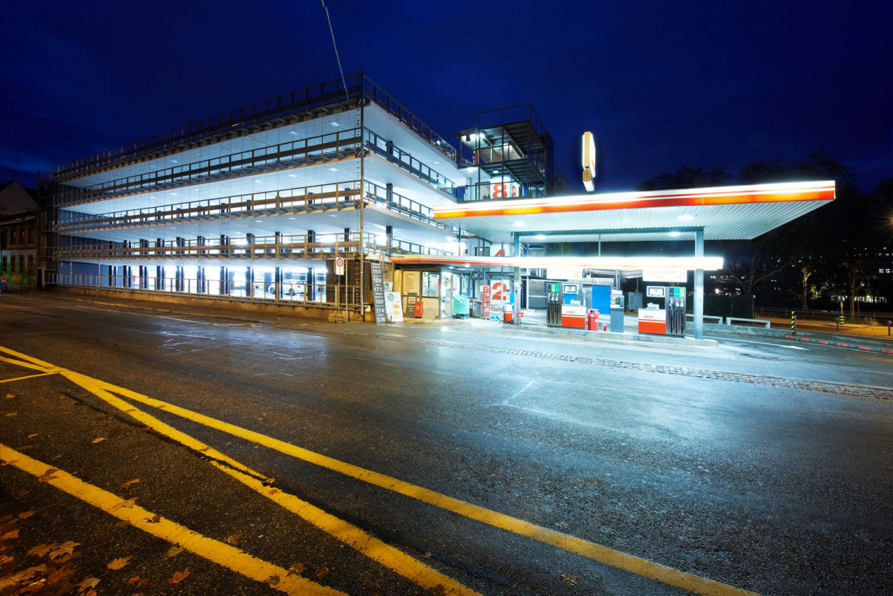 Parrkhaus neben geld-orange beleuchteter Tankstelle in der Nacht.