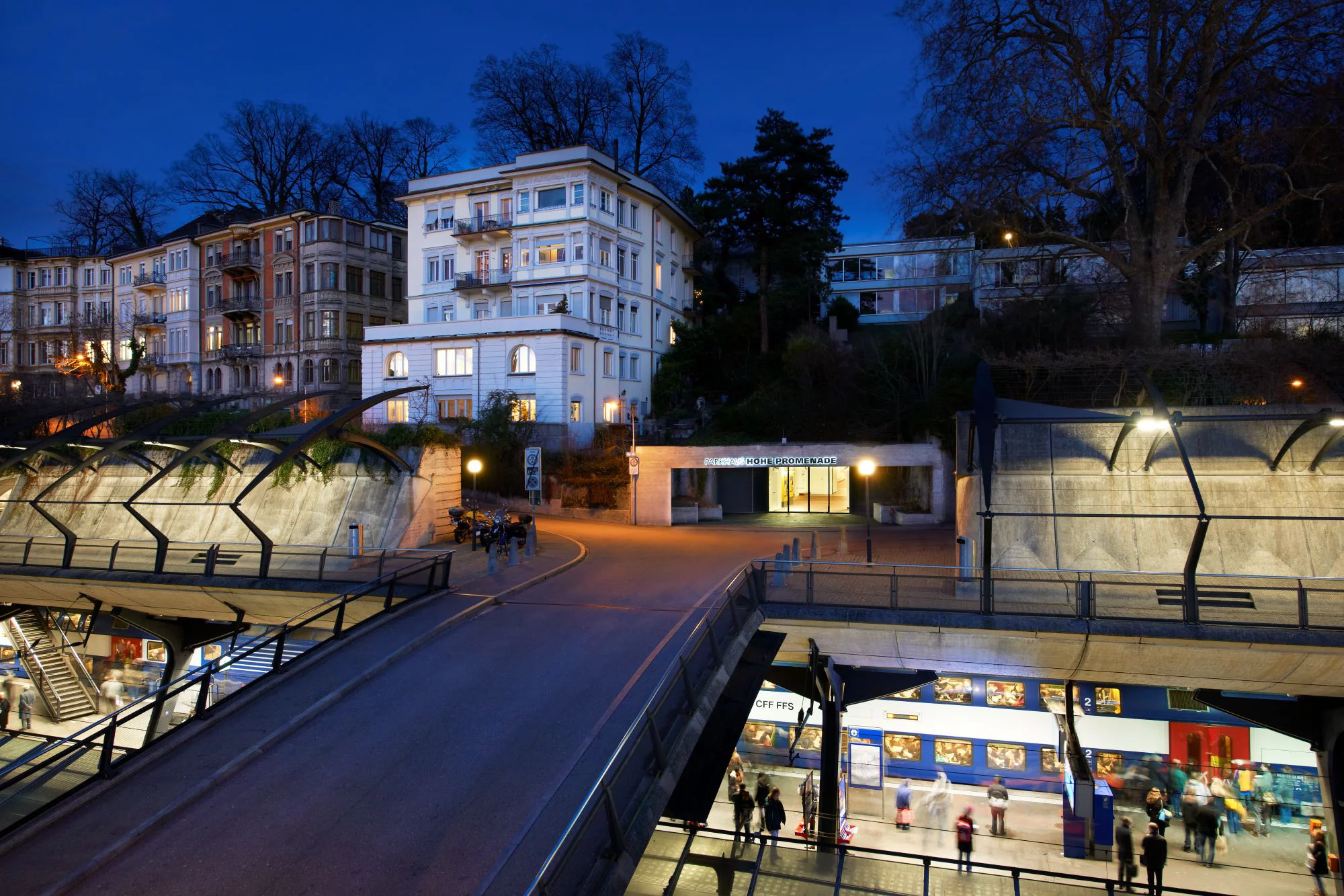 Parkhauseingang oberhalb eines Bahnhofs, in der ein blau-weisser Zug steht. Bild: Luca Zanier