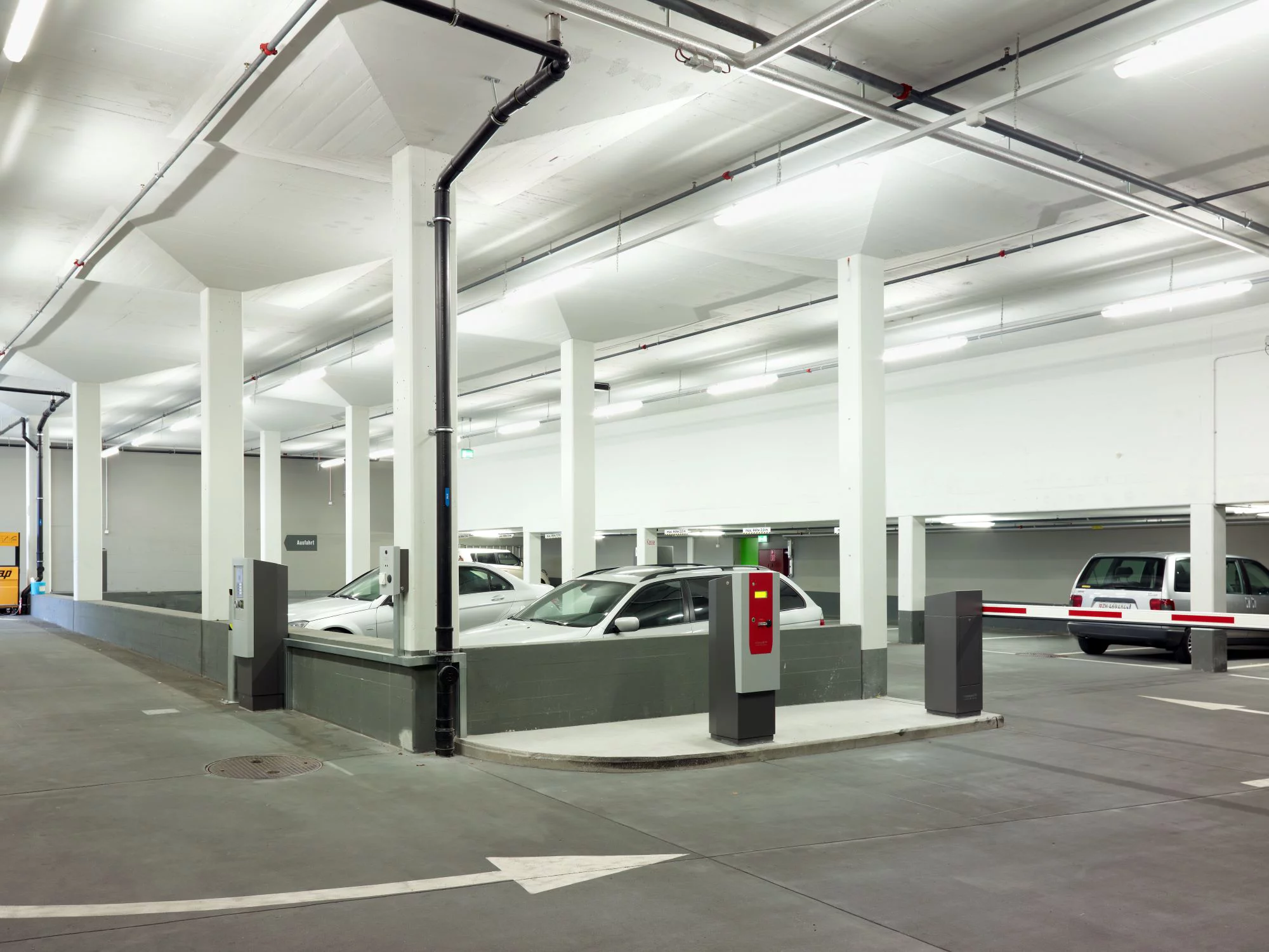 Weisse Autos, in einem Parkhaus mit dunklem Boden und einer Schranke. Bild: Luca Zanier