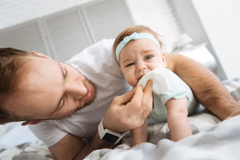 Ein Vater reinigt behutsam den Mund seines Babys mit einem Tüchlein.