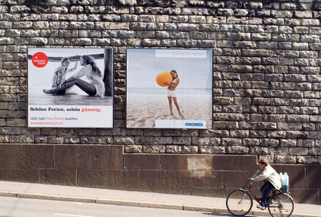 Plakate an der Wand nähe Central und eine Frau auf dem Velo