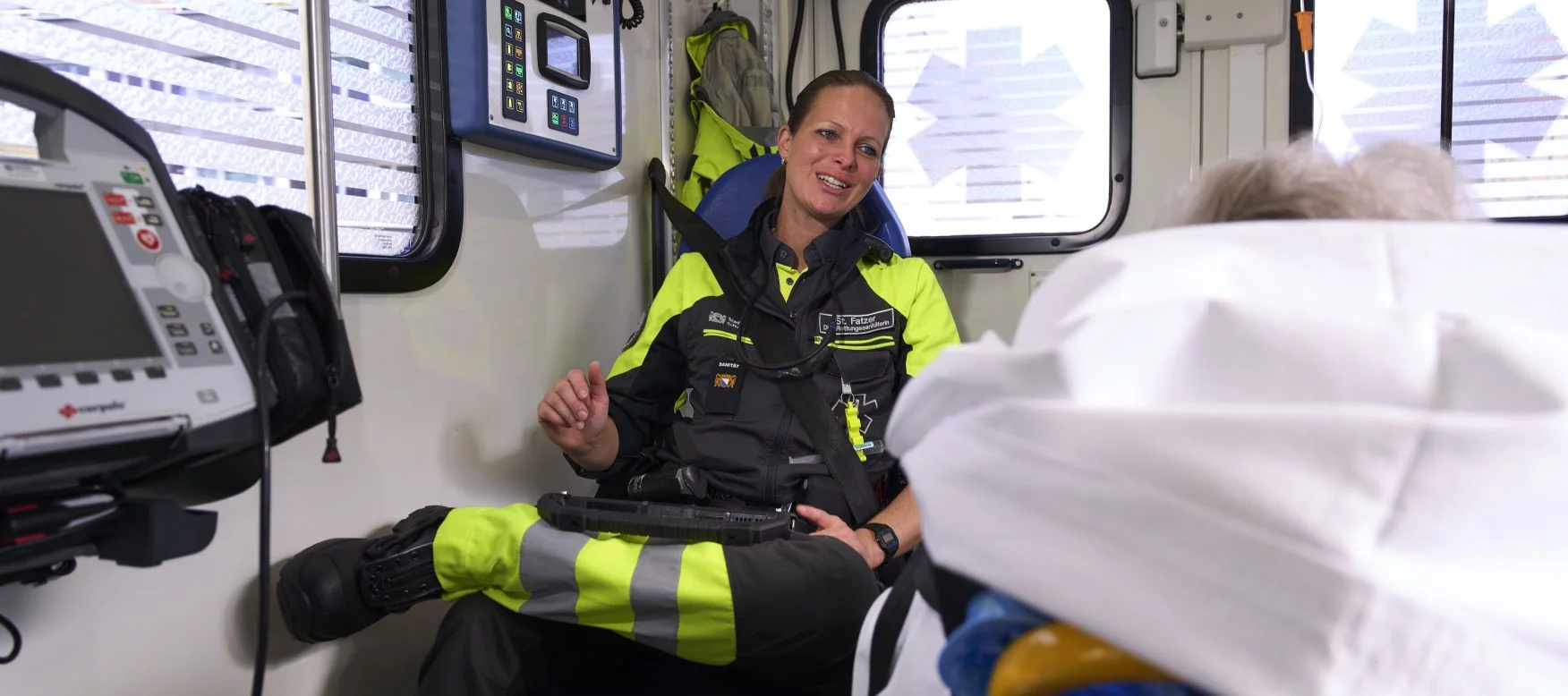 Eine Rettungssanitäterin spricht im Rettungswagen mit einem älteren Patienten.