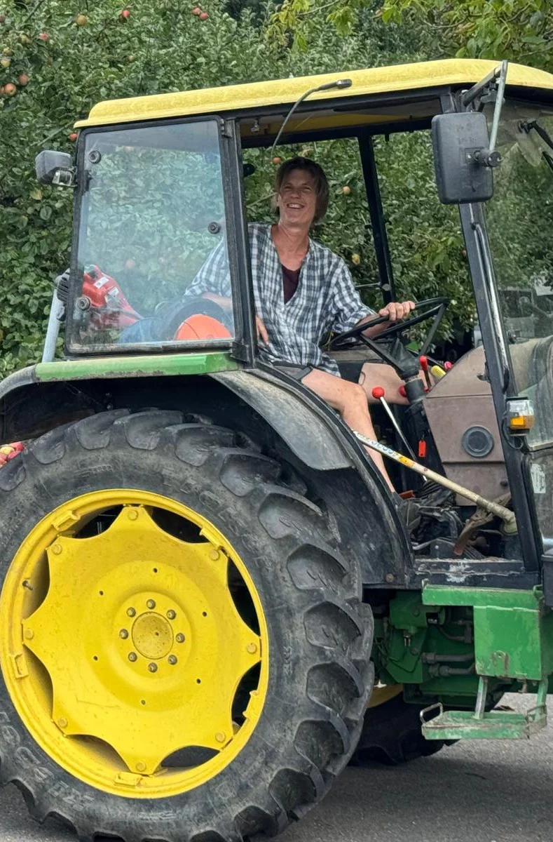 Man sieht Bettina Wolfgramm. Sie sitzt am Steuer eines Traktors mit gelbem Dach und gelben Felgen.