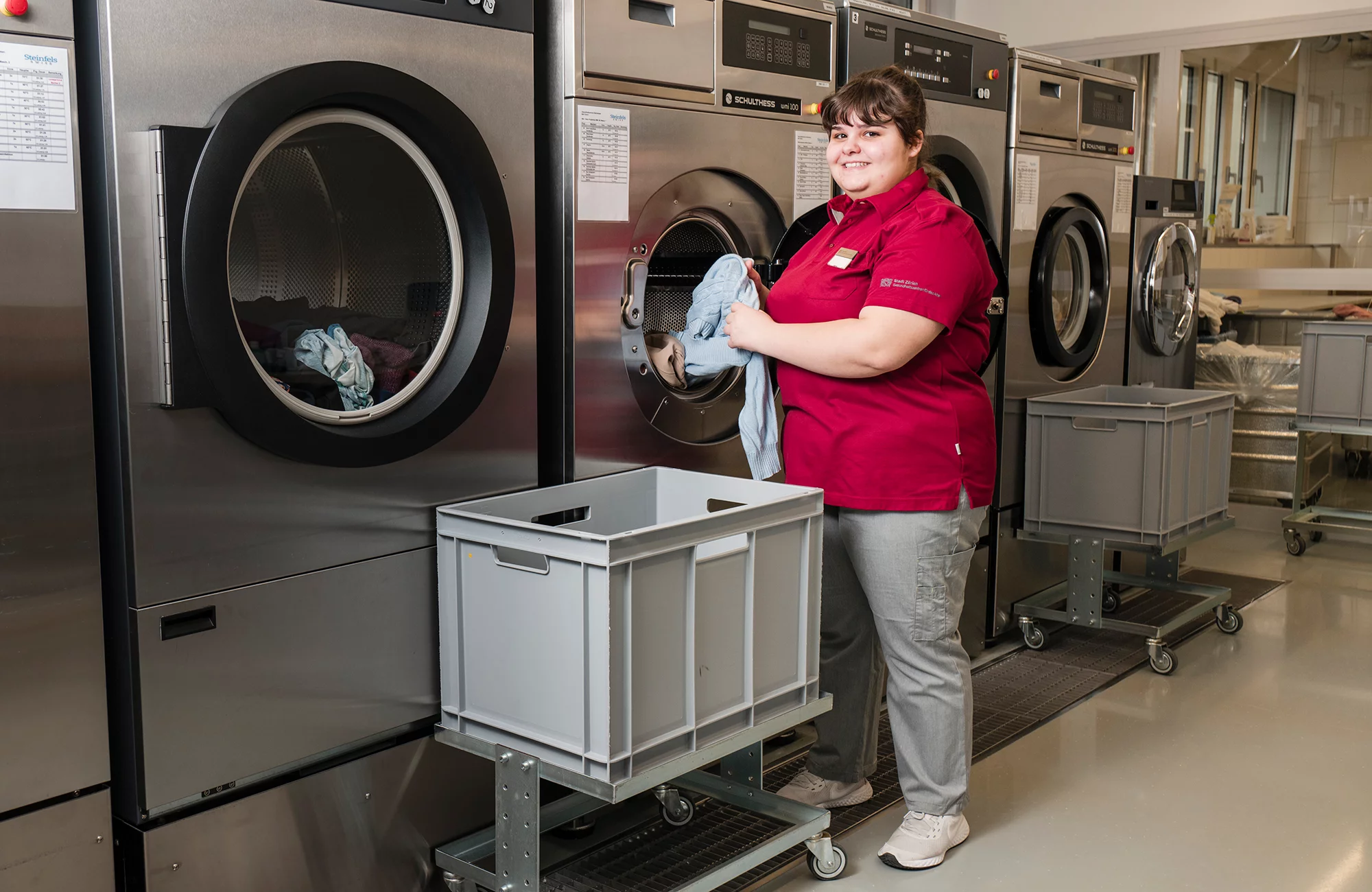 Eine Praktikerin Hotellerie-Hauswirtschaft in Ausbildung steht in der Wäscherei vor einer Waschmaschine.