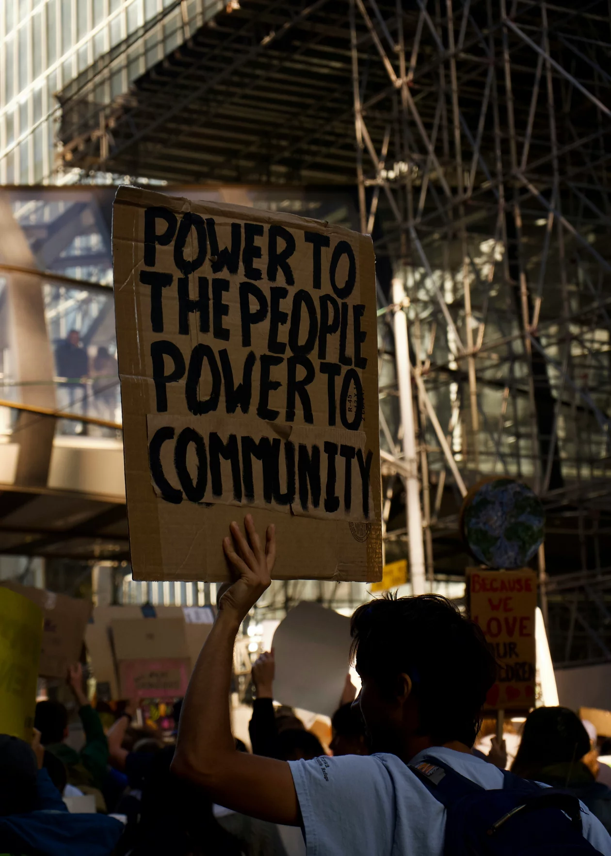 Ein Foto einer Demonstation. Ein Mann hält ein Plakat mit dem Text «Power to the People, Power to Community» hoch.