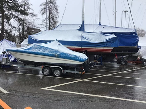 Auf den mit Planen bedeckten Schiffen, die auf Fahrzeuganhängern stehen, liegt Schnee