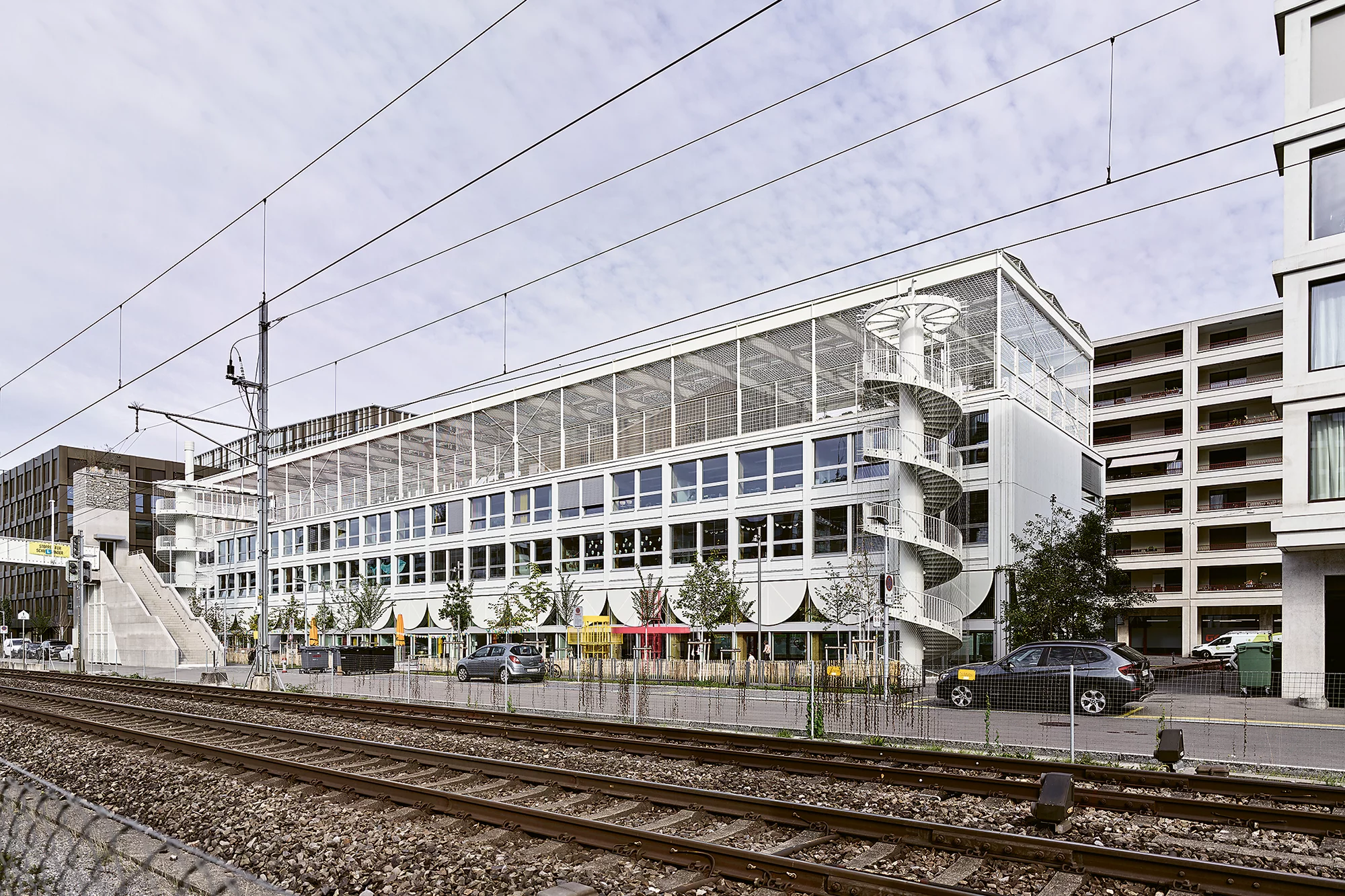 Das Foto wirft einen Blick über die Gleise der Limmatbahn auf das Gebäude der Schulanlage mit der Passerelle Haspelsteg im Hintergrund.