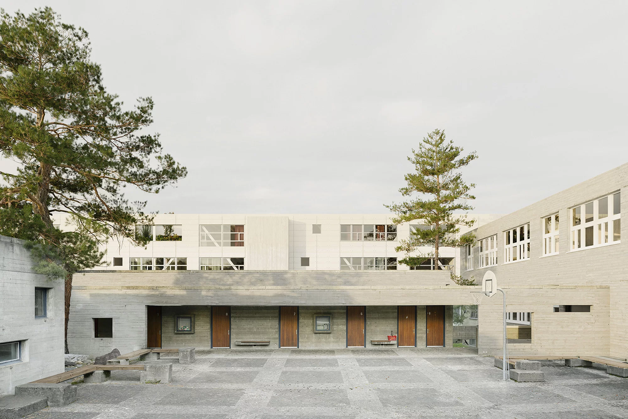 Innenhof des Schulgebäudes mit Bäumen, Sitzbänken, Türen und Basketballkorb.