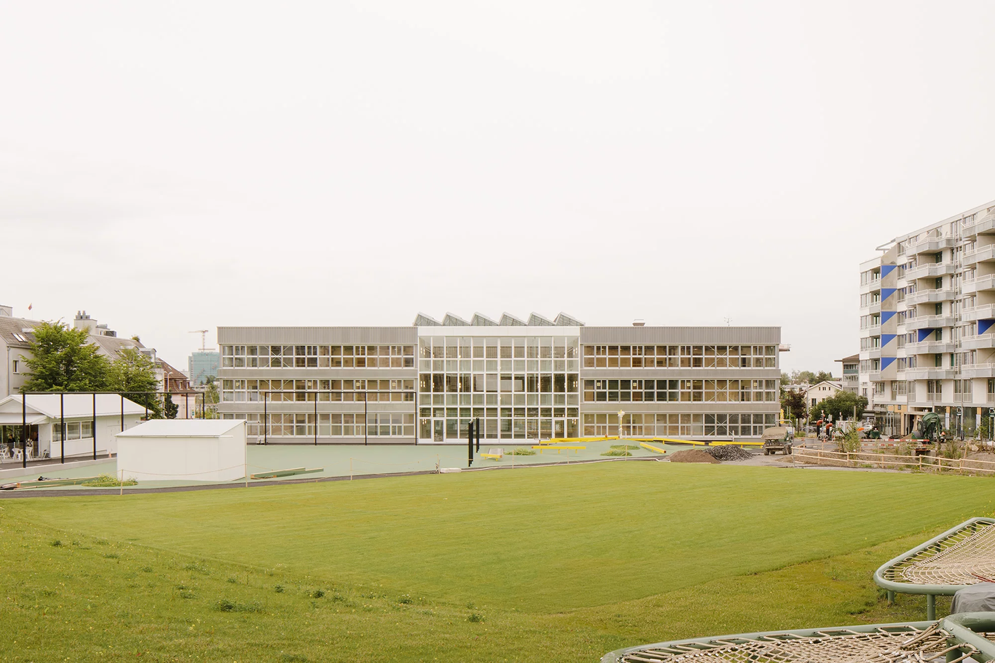 Das Foto wirft einen Blick über die grüne Wiese auf das Gebäude der neuen Schulanlage.