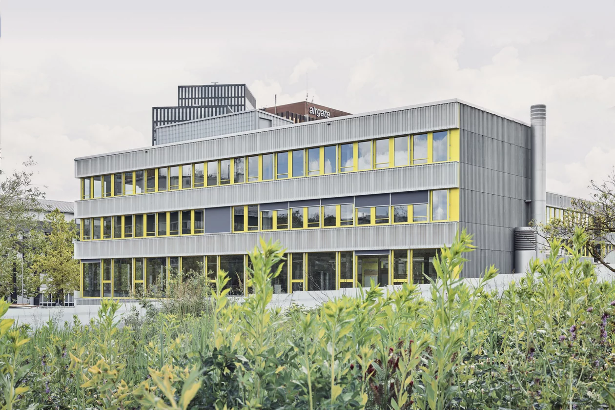 Das Foto wirft einen Blick von der grünen Umgebung auf die Fassade der neuen Schulanlage.