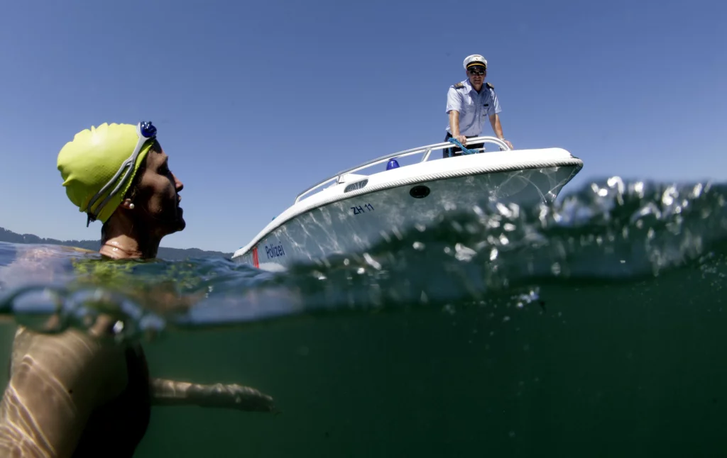 Ein Wasserpolizist spricht vom Boot aus mit einer schwimmenden Person