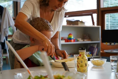 Eine Mitarbeiterin hilft einem Jungen beim Essen