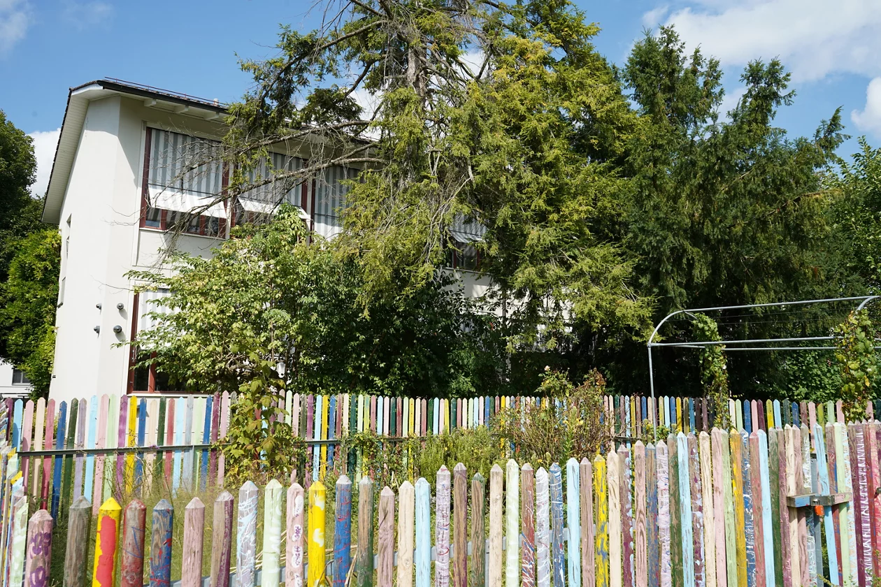 Foto der Fassade der SKB mit einem bunt bemalten Zaun im Vordergrund.