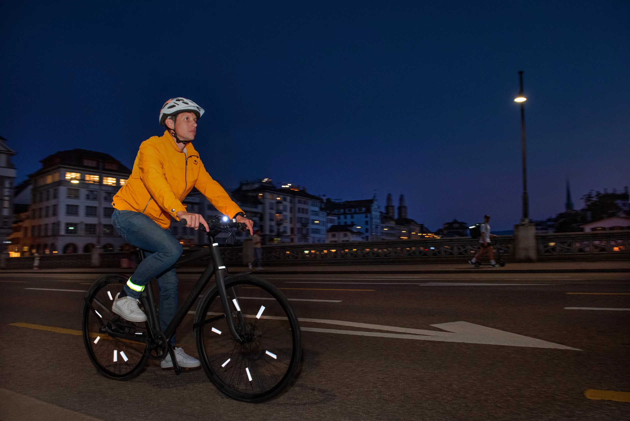Gut sichtbarer Fahrradfahrer mit reflektierender, gelber Jacke und fluoreszierenden Speichenreflektoren, der Nachts unterwegs ist.