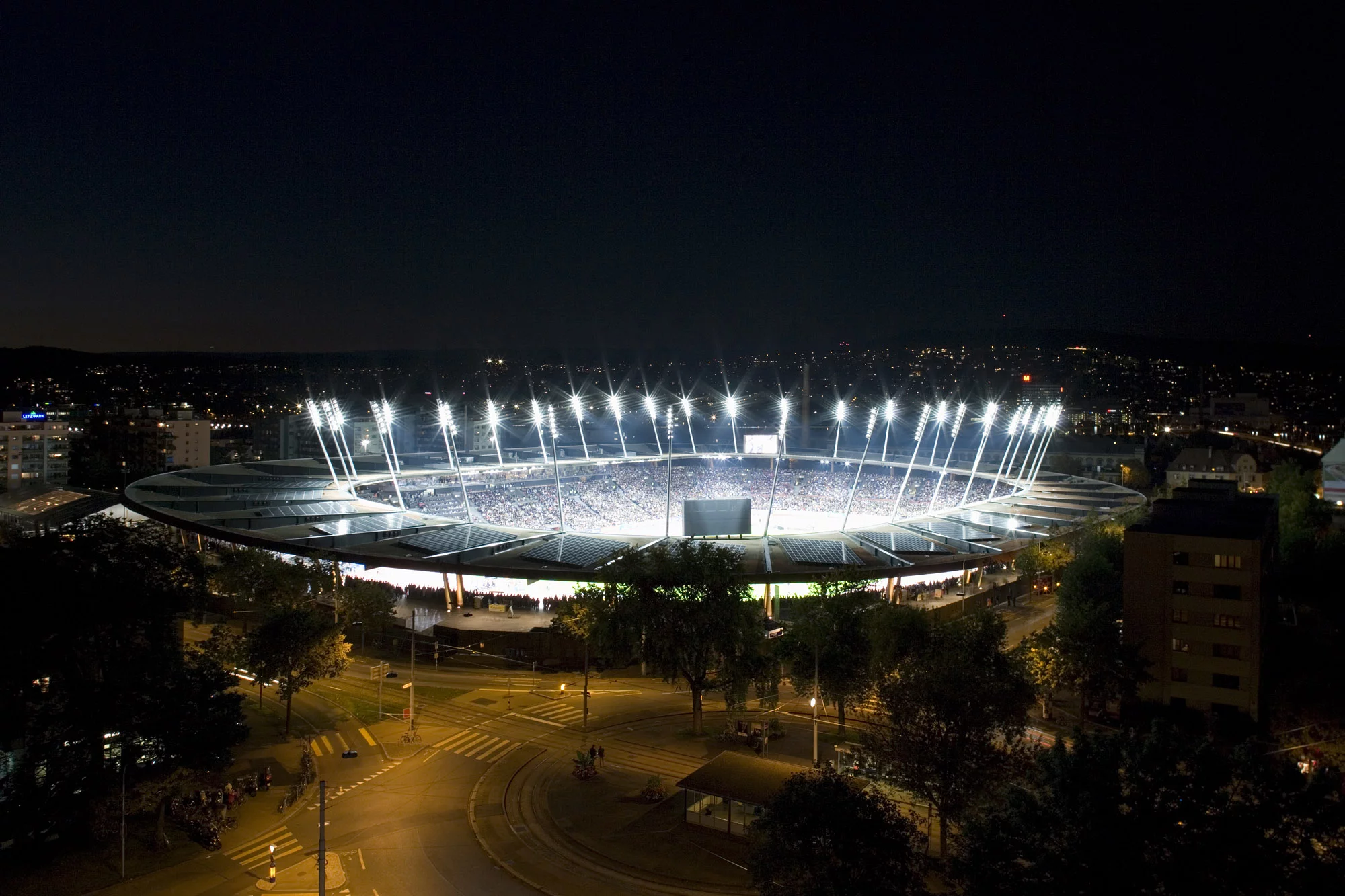 Das Foto wirft einen Blick auf das beleuchtete Stadion in der Nacht mit urbaner Umgebung.