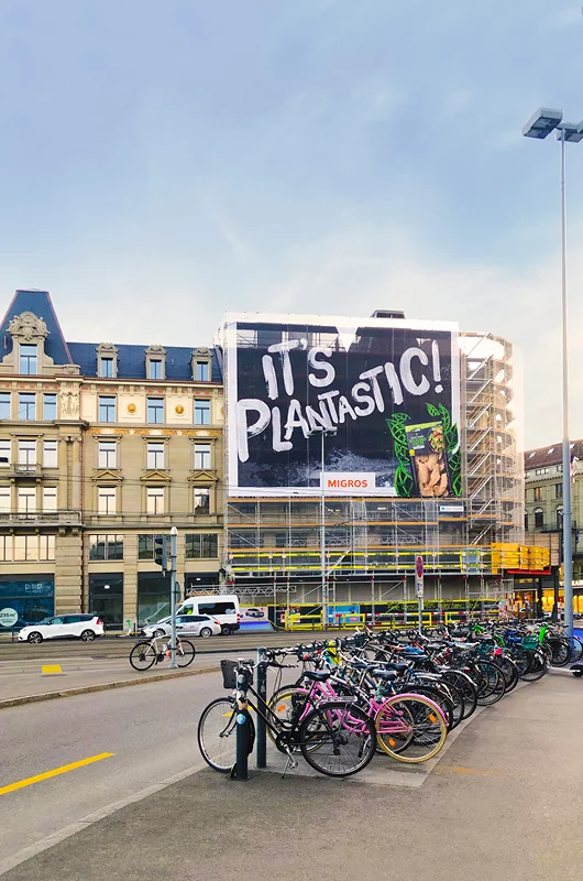 Eine grosse Strassenreklame ist  an einem Gebäude angebracht. 