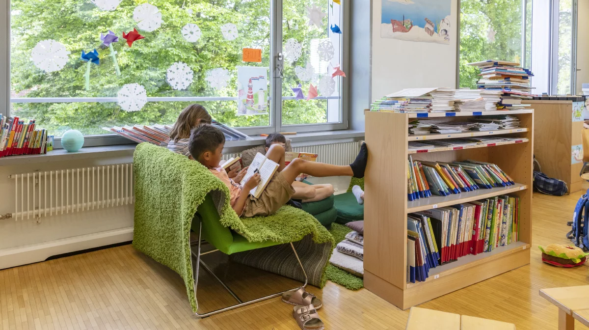 Foto: Ein Mädchen und ein Junge sitzen auf einem grünen Sofa und lesen in Büchern.