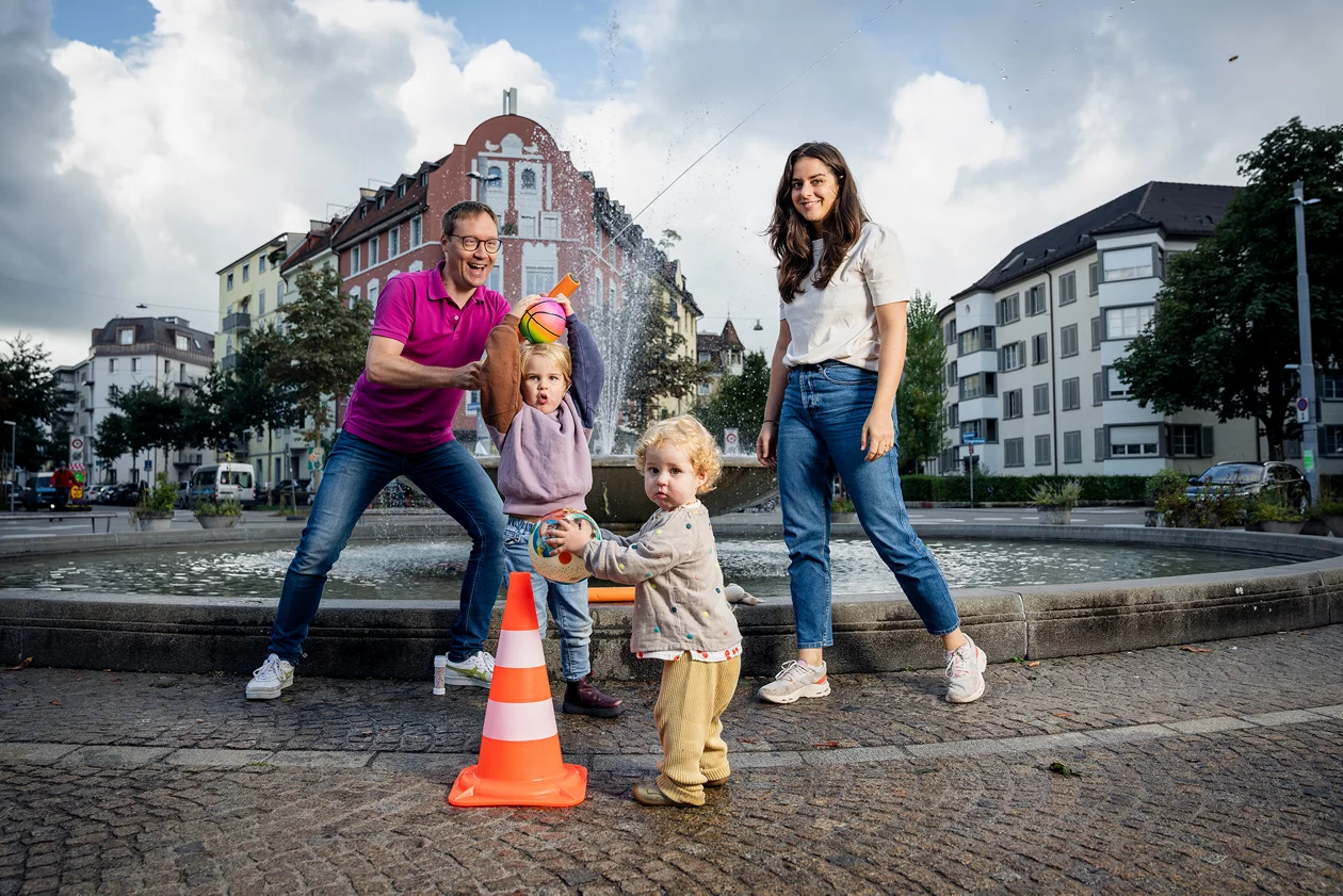 Eine Familie mit Kleinkindern vor Brunnen auf städtischem Platz.