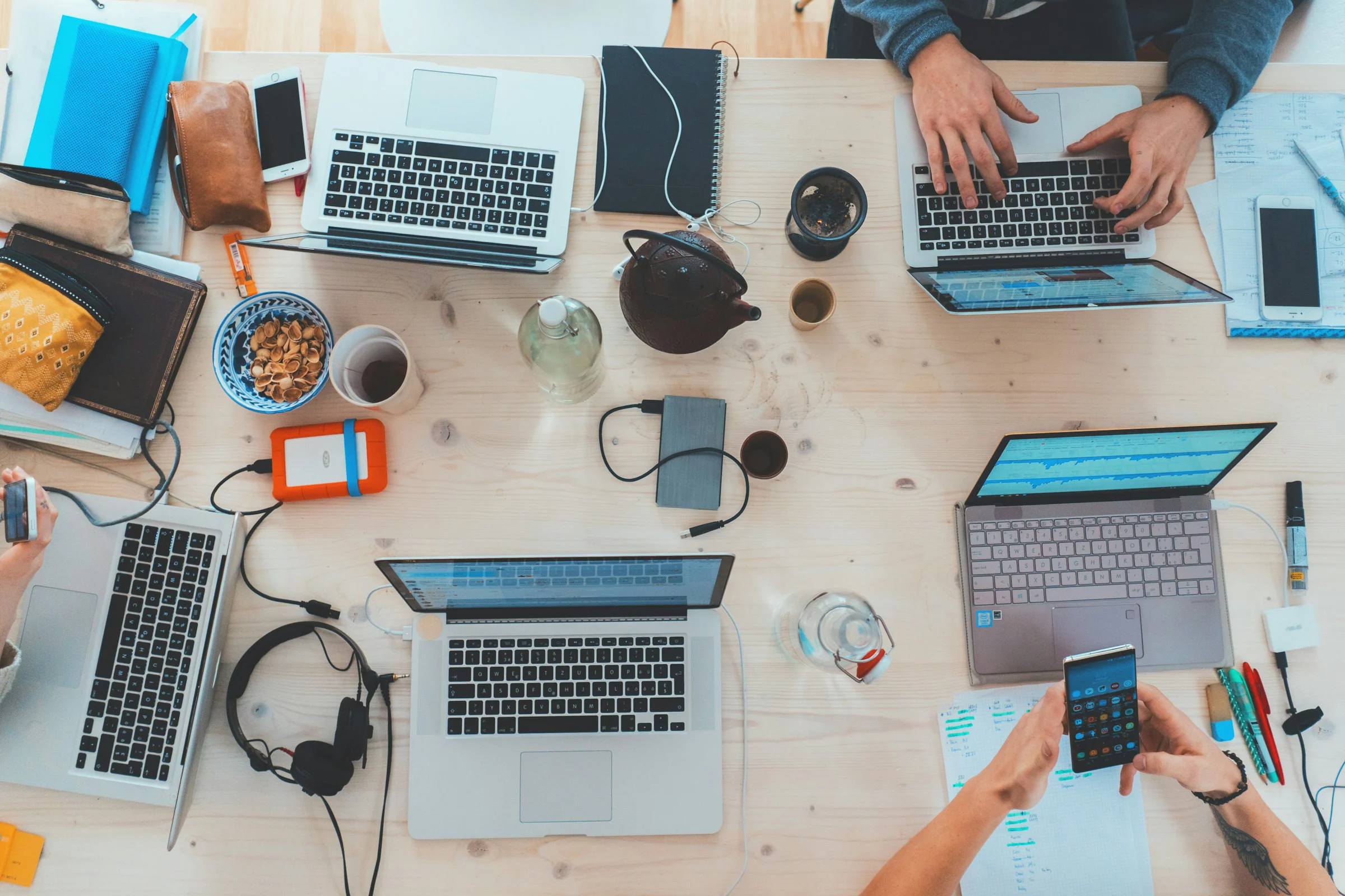 Blick von oben auf einen Tisch mit vielen Laptops und arbeitenden Menschen