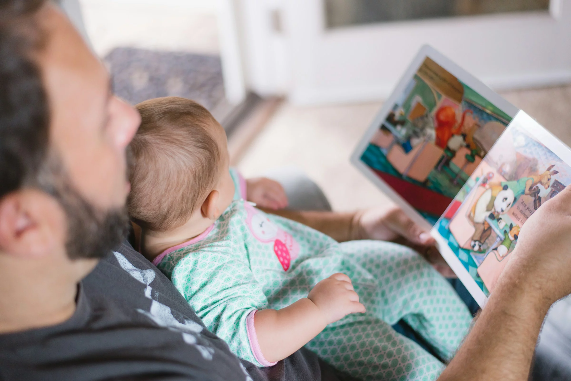 Kind liegt auf dem Bauch eines Mannes und schaut sich ein Kinderbuch an