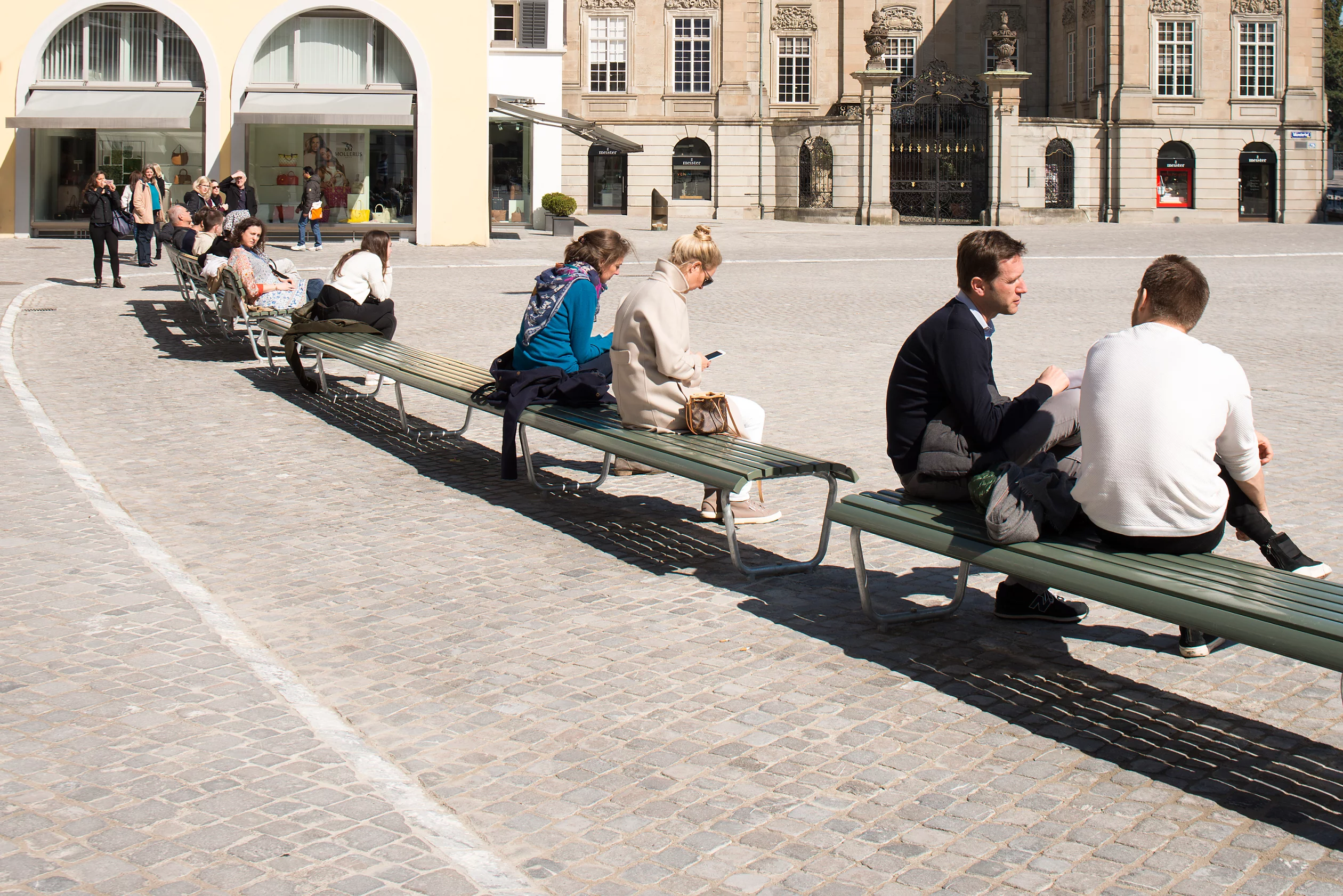 Personen sitzen auf Bänken auf dem Münsthofplatz