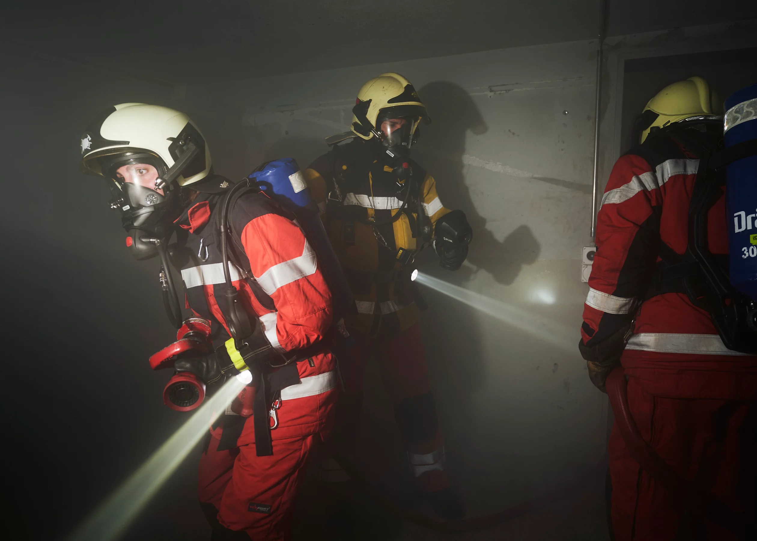 Feuerwehrleute mit Atemschutz untersuchen einen verrauchten Raum.