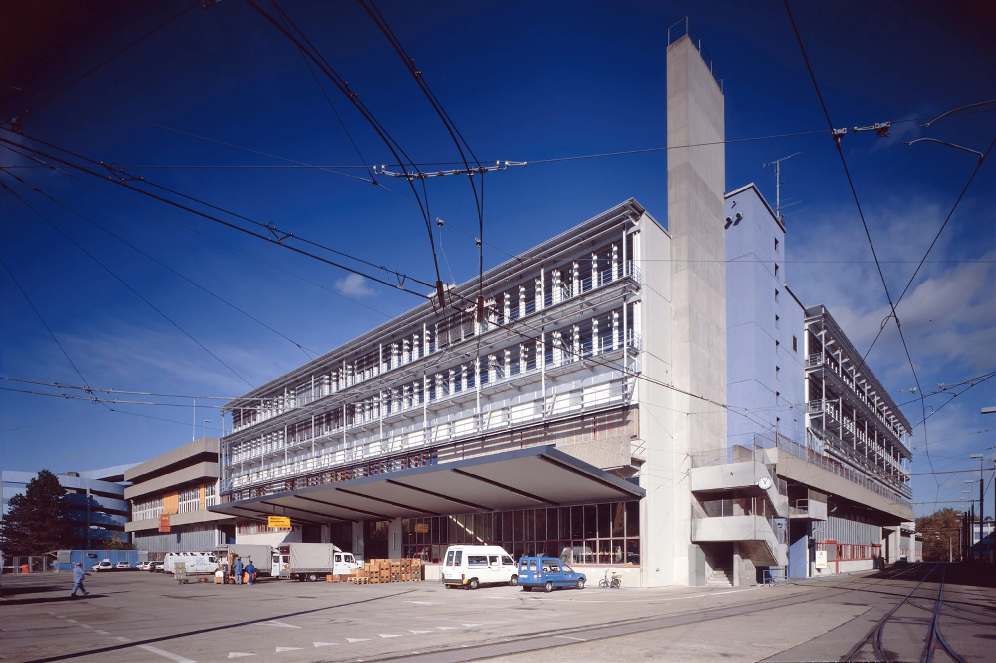 Grosses helles Gebäude der VBZ Zentralwerkstatt an einer Strasse mit Tramleitungen im Vordergrund.